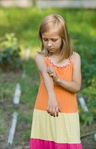 Ein Mädchen im Sommerkleid kratzt sich am Arm