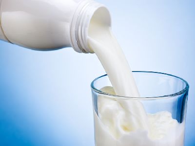 Aus weißer Milchflasche fließt Milch in ein Glas vor hellblauem Hintergrund