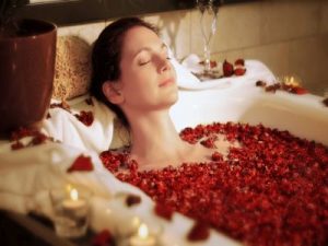 Eine Frau liegt in einer Badewanne mit Kerzenlicht und Rosenblättern