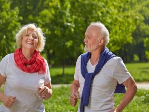 Zwei lächelnde Senioren joggen gemeinsam in der Natur im Sommer