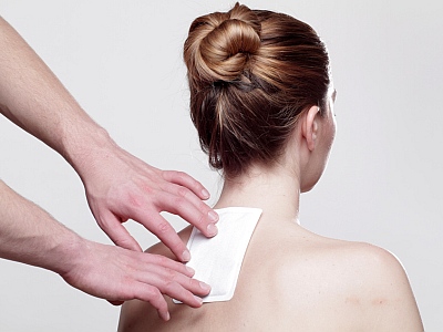 Einer Frau wird ein medizinisches Pflaster auf den Rücken geklebt.