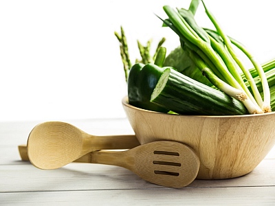 Eine Holtschüssel mit grünem Gemüse und Holzsalatbesteck.