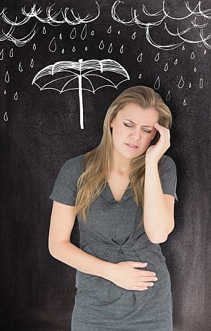 Eine Frau mit Kopf und Bauchschmerzen vor einer Wand mit Zeichnungen von Regen und Regenschirm.