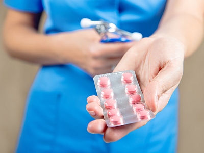 Eine Ärztin in blauem Kittel hält Tabletten in der Hand.