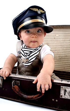 Ein Kind mit Pilotenkappe sitzt im Koffer.