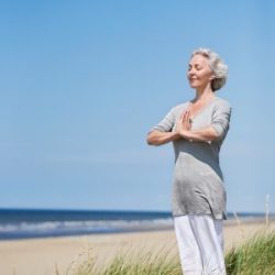 ältere Frau meditiert am Strand