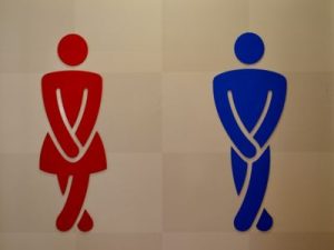 Toilettenzeichen, rot Frau, blau Mann, beide mit verschränkten Beinen