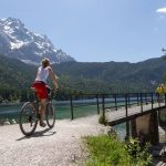 Jüngere Frau auf Bike vor dem überqueren einer Brücke über einen See vor Bergkulisse