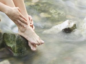 Eine Frau taucht ihre Füße in einen Waldbachlauf.