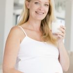 Eine schöne, schwangere blonde Frau lächelt und trinkt ein Glas mit Milch.