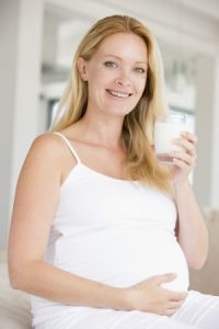 Eine schöne, schwangere blonde Frau lächelt und trinkt ein Glas mit Milch.