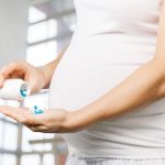 Eine schwangere Frau schüttelt sich Medikamente in die Hand.