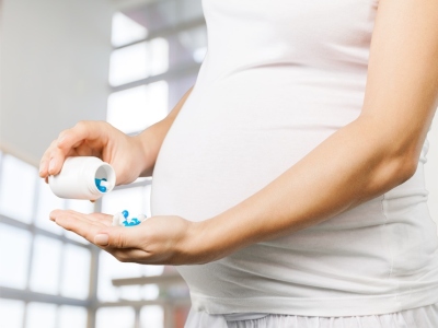 Eine schwangere Frau schüttelt sich Medikamente in die Hand.