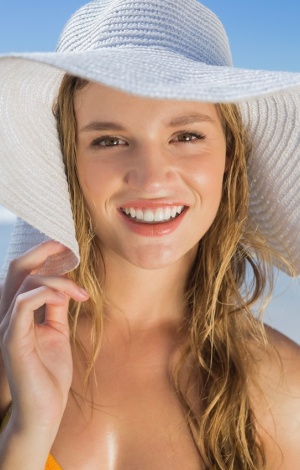 Eine junge blonde Frau schützt sich mit einem weissen Hut.