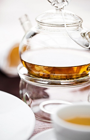 Eine gläserne Kanne mit Tee auf einem Stövchen und eine Teetasse.