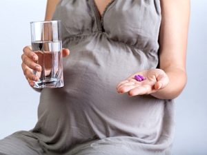 Eine schwangere Frau mit einem Glas Wasser und Medizin in der Hand.