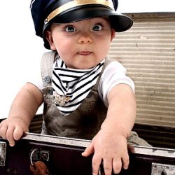 Ein Kind mit Pilotenkappe sitzt im Koffer.