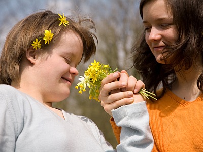 Ein behindertes Kind mit gesunder Schwester schnuppern an Blumen.