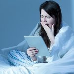 Eine Frau sitzt im Bett und liest in einem e-reader.