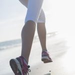 Die Beine einer sportlichen Frau, die am Strand joggt.