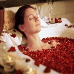 Eine Frau liegt in einer Badewanne mit Kerzenlicht und Rosenblättern