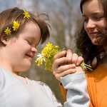 Ein behindertes Kind mit gesunder Schwester schnuppern an Blumen.