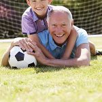 Opa und Enkel spielen fröhlich mit dem Fußball.