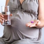 Eine schwangere Frau mit einem Glas Wasser und Medizin in der Hand.